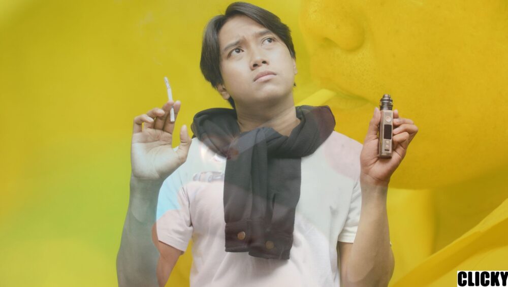 Seorang lelaki memegang rokok dan alat vape sedang memikirkan Akta 852 Malaysia